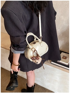 Detail of cream white Boston bag with gold rivets and a brown teddy bear charm