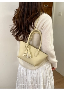 Creamy yellow bucket bag with tassel detail worn by model in minimalist retro style