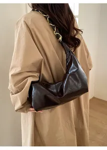 Detail of dark brown glossy leather shoulder bag with gold chain strap on model