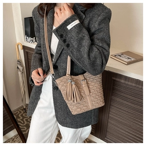 Detail of beige pleated woven bucket bag with tassel charms and adjustable shoulder strap