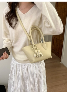 Beige bucket bag with fringe detail and pebbled leather texture on a white outfit