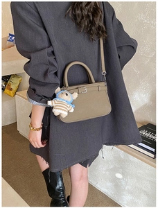 Detail of khaki textured leather handbag with metal buckle and teddy bear charm