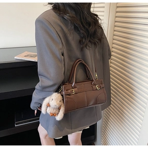 Detail of dark brown retro crossbody bag with plush bunny charm on a gray blazer model