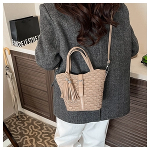 Detail of a beige woven bucket bag with elegant 3D geometric texture and tassel