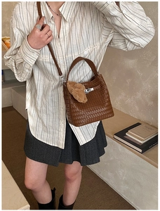 Detail of woven brown bucket bag with metal turn-lock closure and plush charm