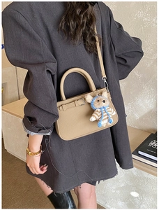 Detail of beige textured leather handbag with a cute teddy bear plush charm and strap