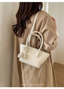 Detailed view of milk white leather bucket bag with tassel charm worn over a trench coat