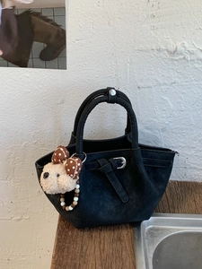 Sac seau plissé noir chic avec breloque ours sur une table en bois rustique