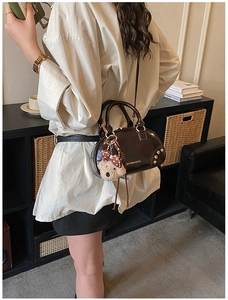 Close-up of brown bowling bag with gold hardware and a cute teddy bear charm detail
