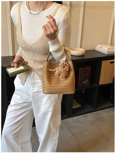 Close-up of woven texture brown bucket bag with a cute plush bear charm accessory