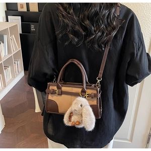 Detail of retro color-block handbag with plush rabbit charm worn on black shirt