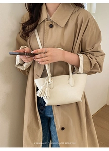 Detail of a minimalist beige bucket bag featuring a leather tassel and textured finish
