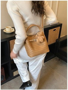Close-up of brown woven bucket bag featuring silver hardware and a cute teddy bear charm