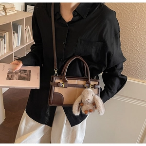 Retro contrast color handbag with plush rabbit charm in a cozy indoor setting