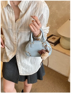 Detail of light blue Boston bag featuring gold rivets and a plush bear charm accessory