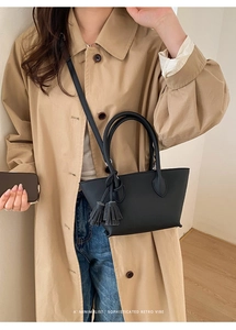 Detail of a minimalist black bucket bag with tassels on a model in a beige trench coat
