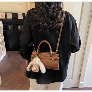 Brown leather handbag with gold buckle detail and white plush rabbit charm on side