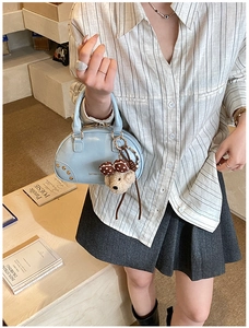 Detail of light blue Boston handbag featuring golden rivets and a plush bear pendant