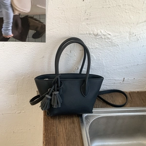 Detail view of black faux leather bucket bag with tassel charms and detachable strap