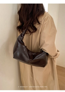 Deep brown crescent hobo bag with retro pleats worn over a trench coat by a model