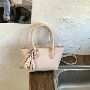 Detail of beige litchi grain bucket bag with tassel charm and dual handles on wood surface