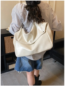 Rear view of model wearing off-white glossy faux leather hobo tote bag with rivet details