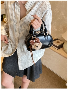 Detail of black glossy handbag with gold rivets and a plush bear charm with polka dot bow