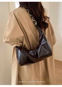 Detail of dark brown glossy leather shoulder bag with golden chain and retro minimalist vibe