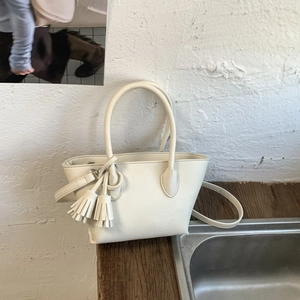 Detail of cream white leather bucket bag with tassels on a wooden surface