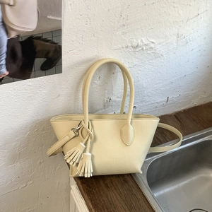 Detail of pale yellow crossbody bucket bag with dual handles and stylish tassel charms