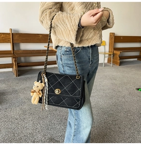 Detail of black quilted crossbody bag with metal twist lock and cute bear charm