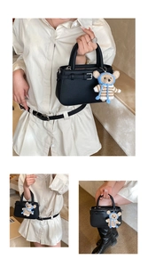 Detail of black litchi grain leather handbag with cute hand-woven teddy bear charm