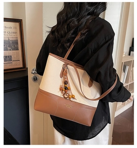 Detail of canvas tote bag with brown leather trim and beaded tassel keychain accessory