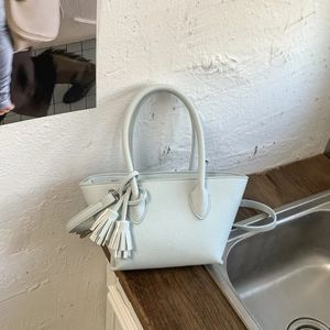Detail of light blue textured leather tote bag featuring round handles and tassel charm