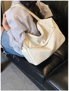 Detail of creamy white tote bag featuring wide laser-cut straps and metallic rivets