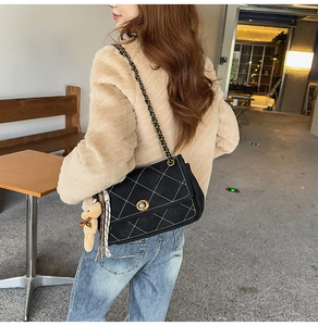 Close-up of black quilted crossbody bag with gold chain strap and teddy bear charm