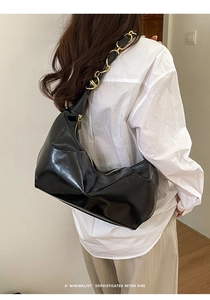 Detail of glossy black shoulder bag featuring gold chain strap and minimalist retro design