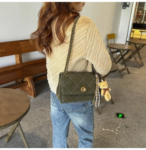 Close-up of green quilted chain bag featuring a pearl-embedded gold clasp and plush bear charm