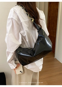 Minimalist black glossy hobo bag with gold chain strap on model in simple interior