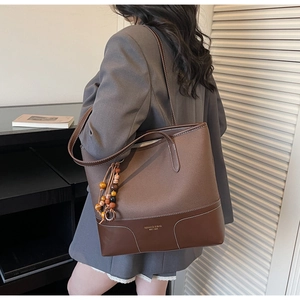 Detail of dark brown canvas tote bag with wooden beads and leather trim on a model