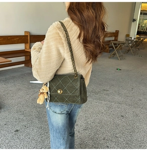 Close-up of olive green quilted suede crossbody bag with golden chain and bear charm