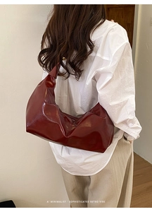 Detail of dark red glossy retro hobo bag showing shoulder carry fit on a model