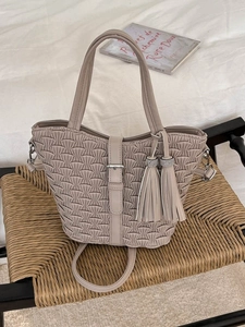 Minimalist beige pleated bucket bag with tassel details and a top handle on a woven chair