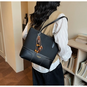 Detail of black leather and canvas tote bag featuring wooden bead tassel and gold branding
