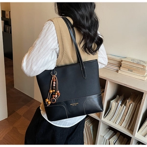 Detail of black tote bag with white stitching, wood beads and tassel charm on a shoulder