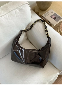 Close-up of retro dark brown hobo bag with woven chain strap on a white sofa
