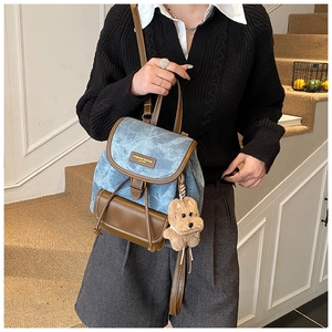 Detail of light blue denim mini backpack with brown leather trim and cute puppy charm