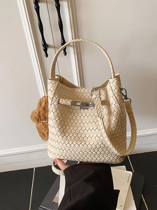 Fashionable beige woven bucket bag with top handle and brown bear charm held by hand