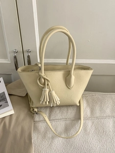 Beige pebble leather bucket bag with top handles, crossbody strap, and tassel charms