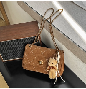 Close-up of brown quilted bag with gold lock, chain strap, and cute bear pendant
